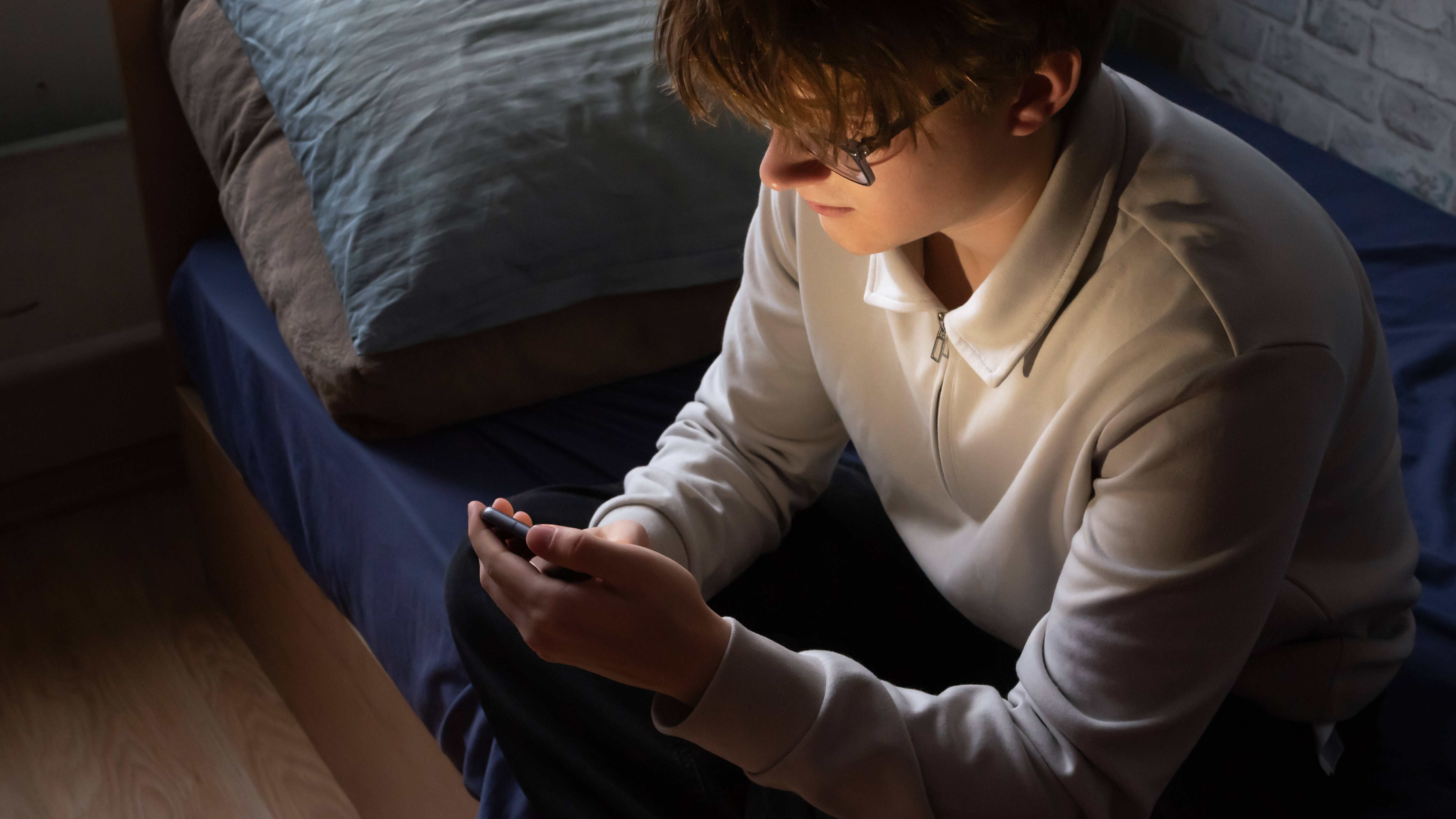 Ein junger Mann sitzt auf seinem Bett und schaut in sein Smartphone