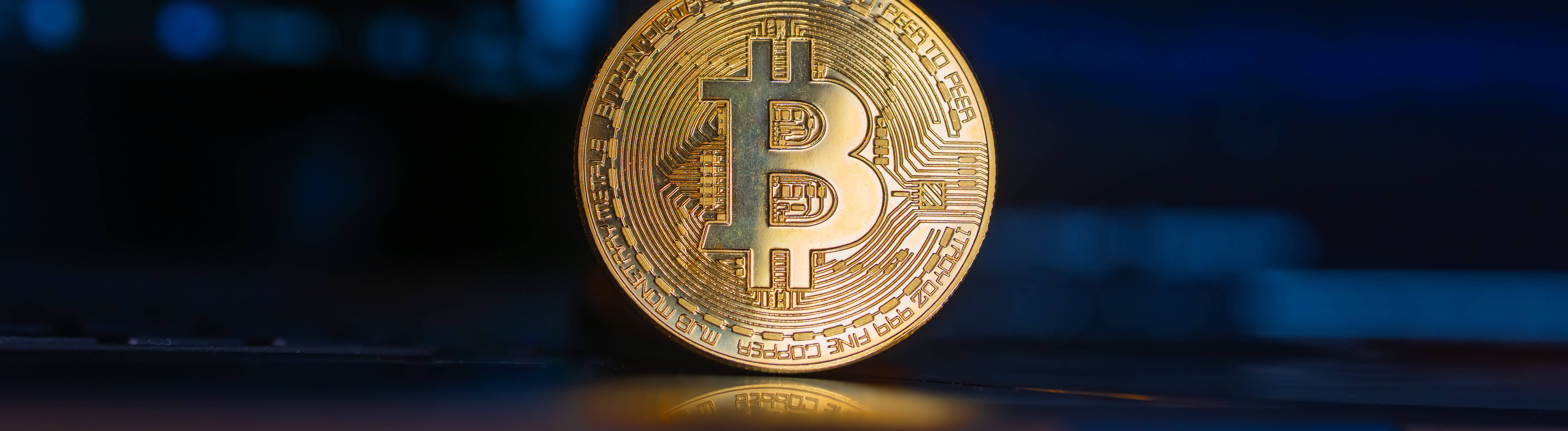 Eine goldene Bitcoin-Münze steht aufrecht vor einem Computer-Bildschirm.