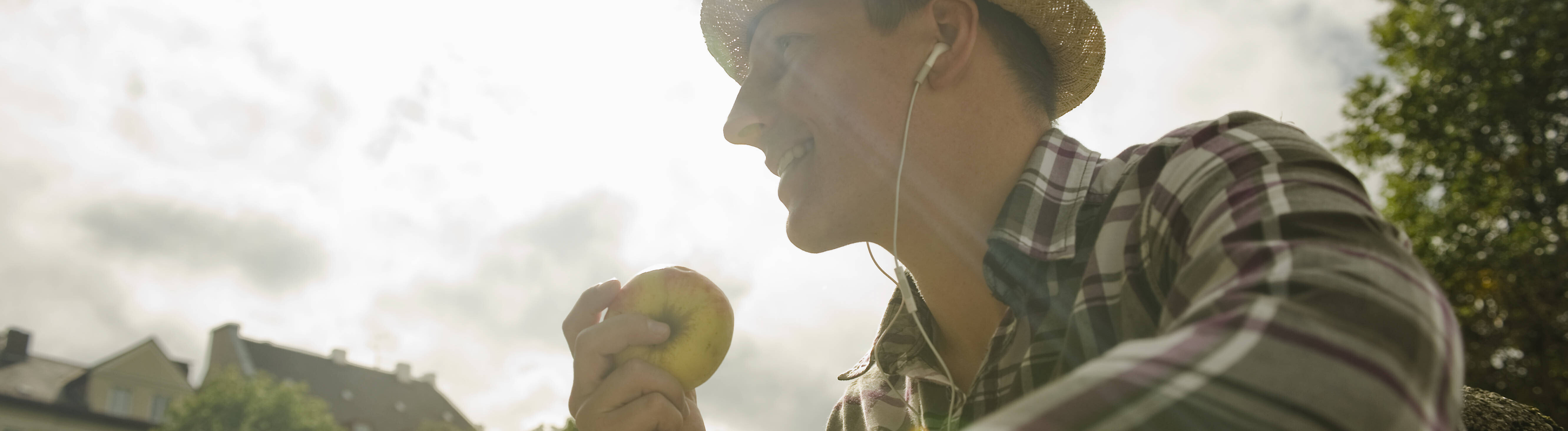 Ein Mann sitzt in der Sonne, trägt einen Strohhut und hält einen Apfel in der Hand (Symbolfoto)
