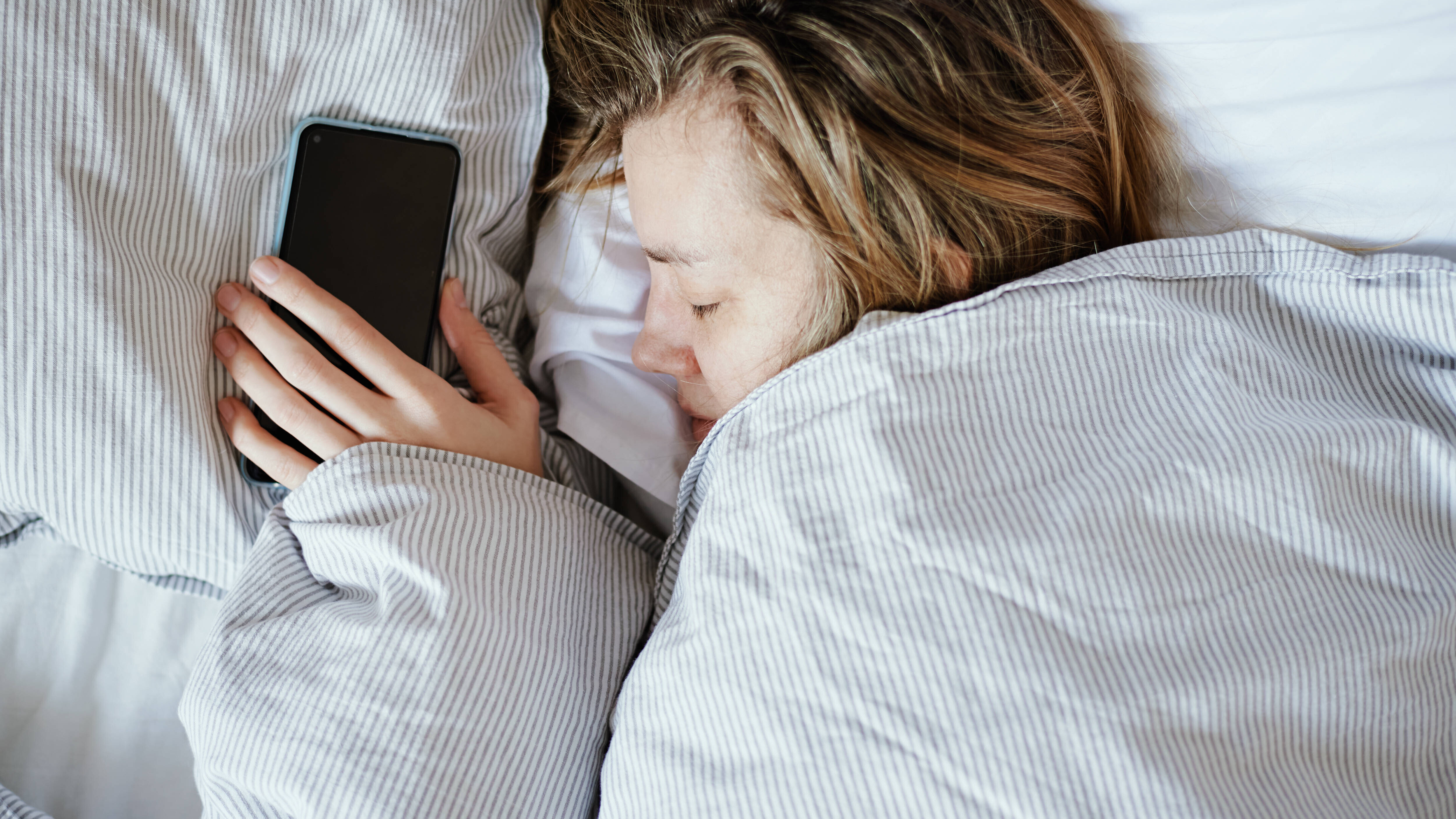 Frau schläft und hält dabei ihr Smartphone in der Hand