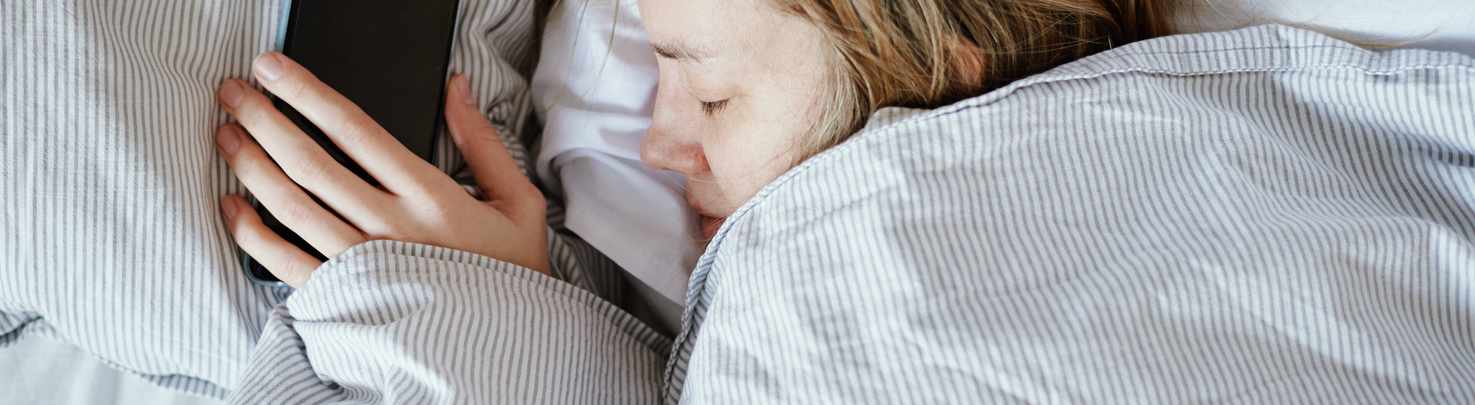 Frau schläft und hält dabei ihr Smartphone in der Hand