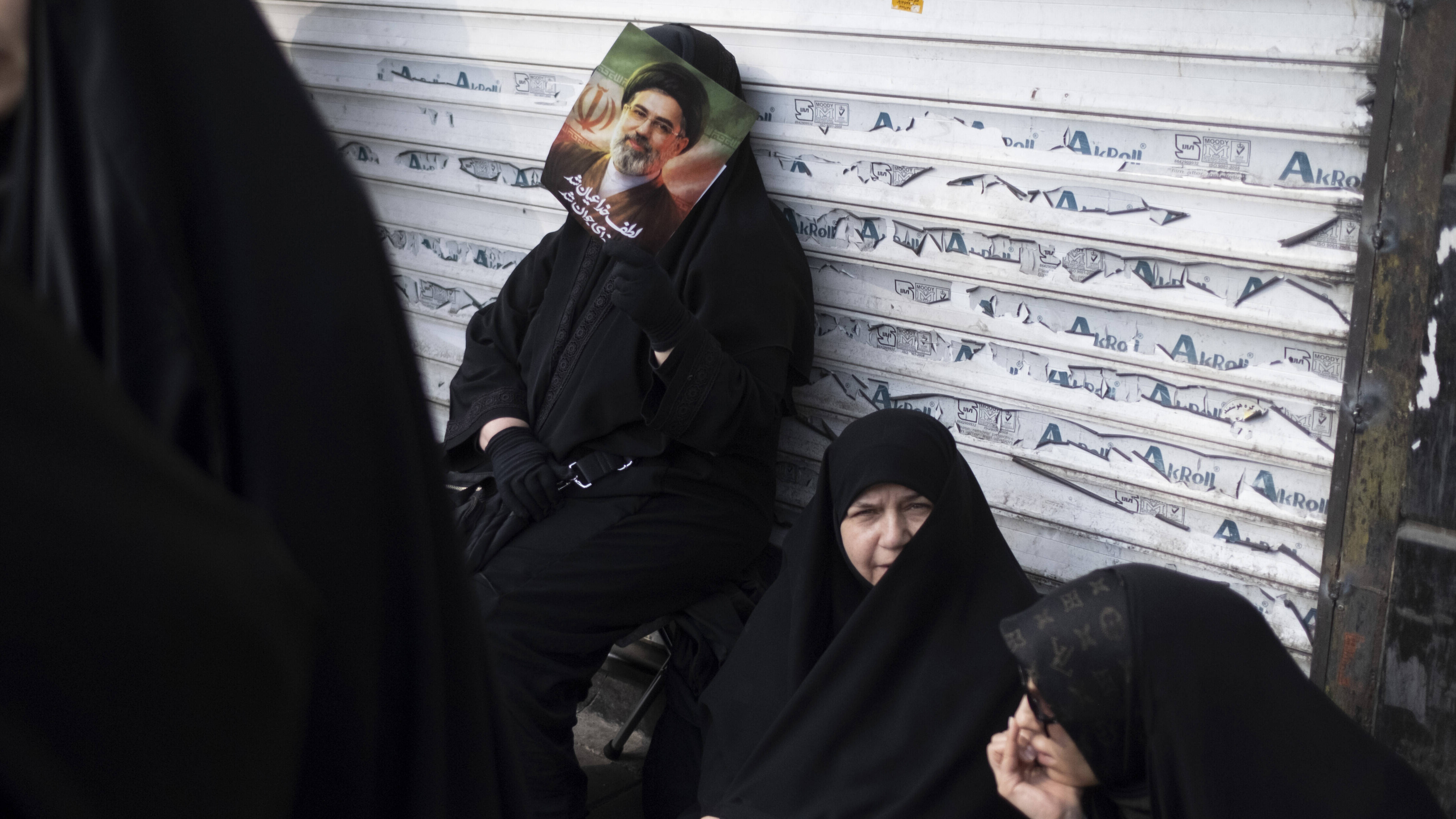 Eine verschleierte Iranerin lehnt sich während einer Jubeldemonstration für Mojtaba Khamenei Anfang März 2026 an die Jalousie eines Geschäfts.