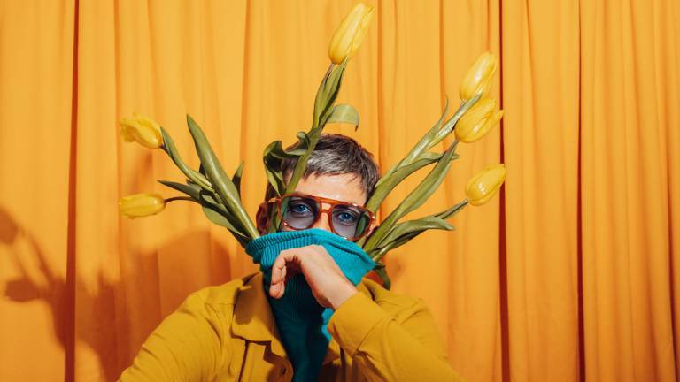 Ein Mann vor einem gelben Hintergrund mit gelben Tulpen in seinem Pullover