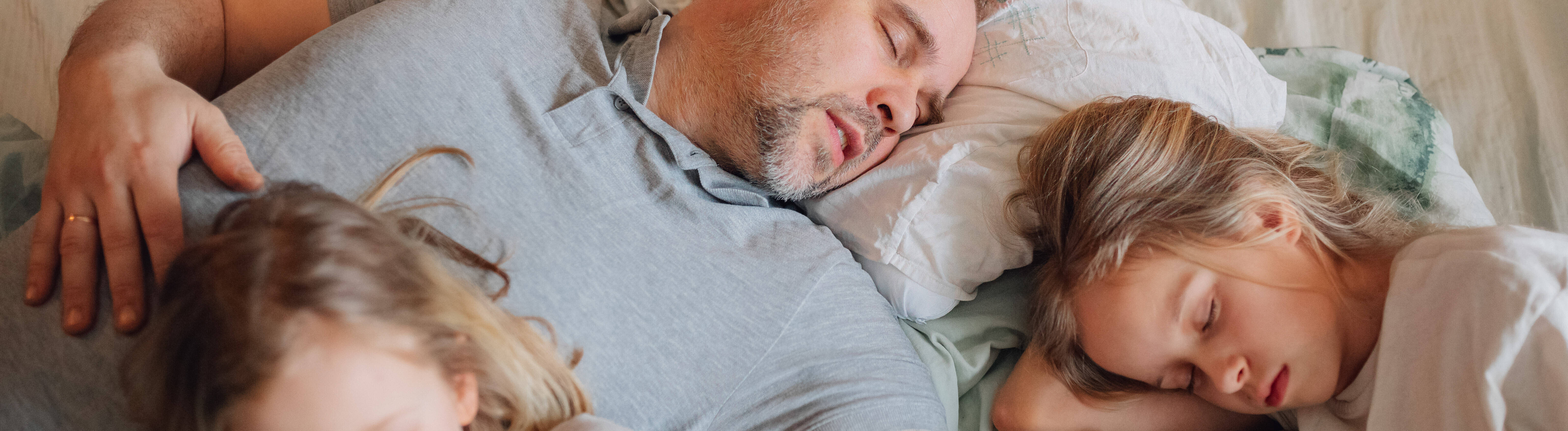 Ein Vater schläft mit seinen zwei Kindern in einem Familienbett.