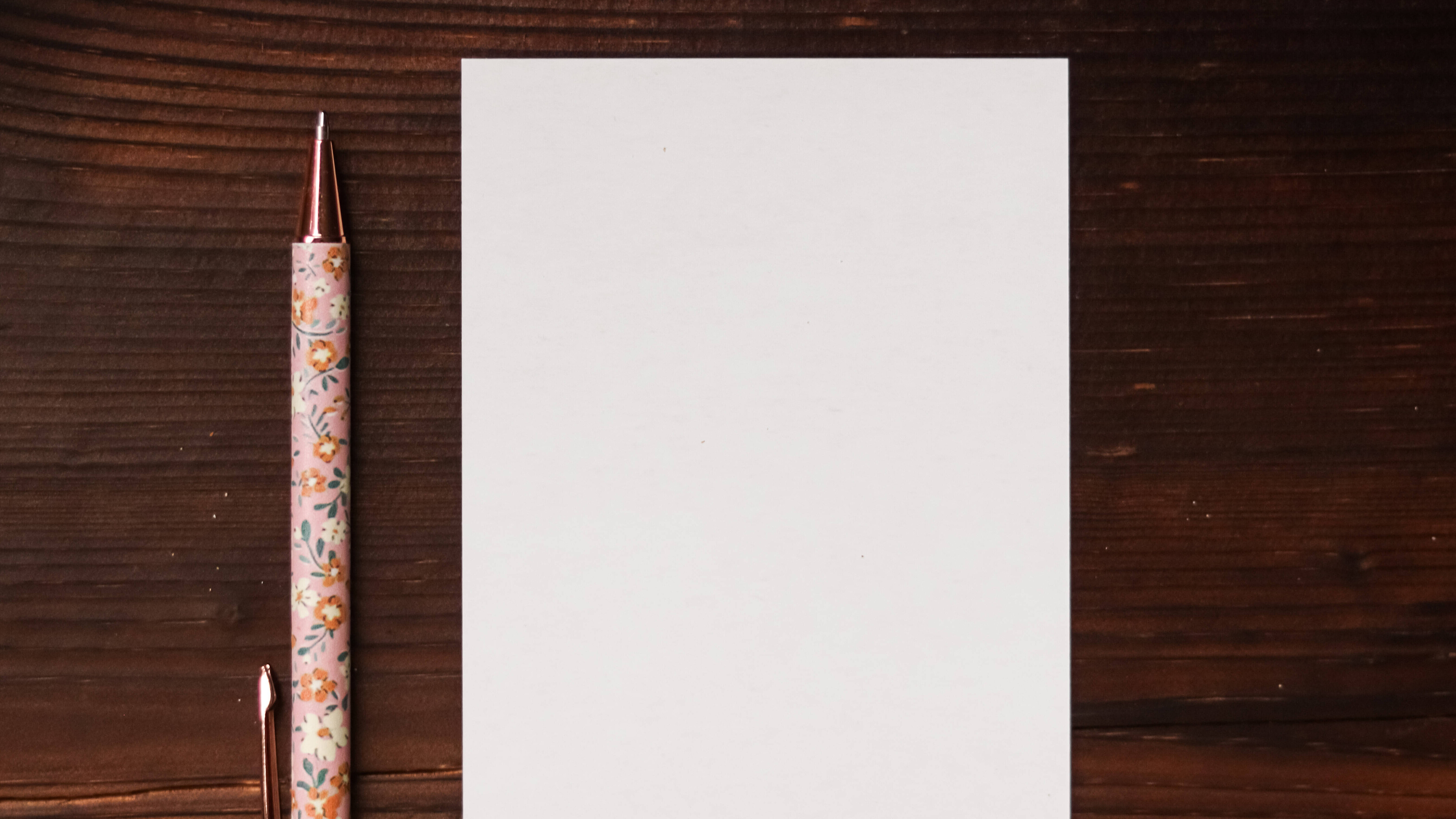 Ein leeres Blatt Papier und ein Kugelschreiber liegen auf einem dunklen Holztisch.