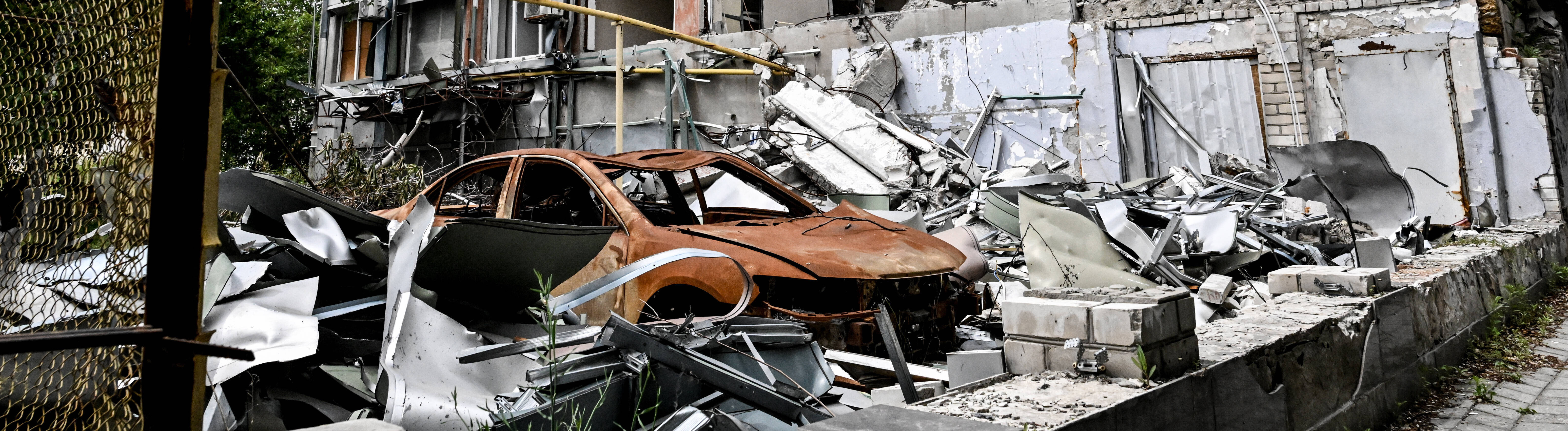Durch russische Angriffe zerstörtes mehrstöckiges Wohnhaus und ausgebranntes rotes Autowrack (10.06.2026)