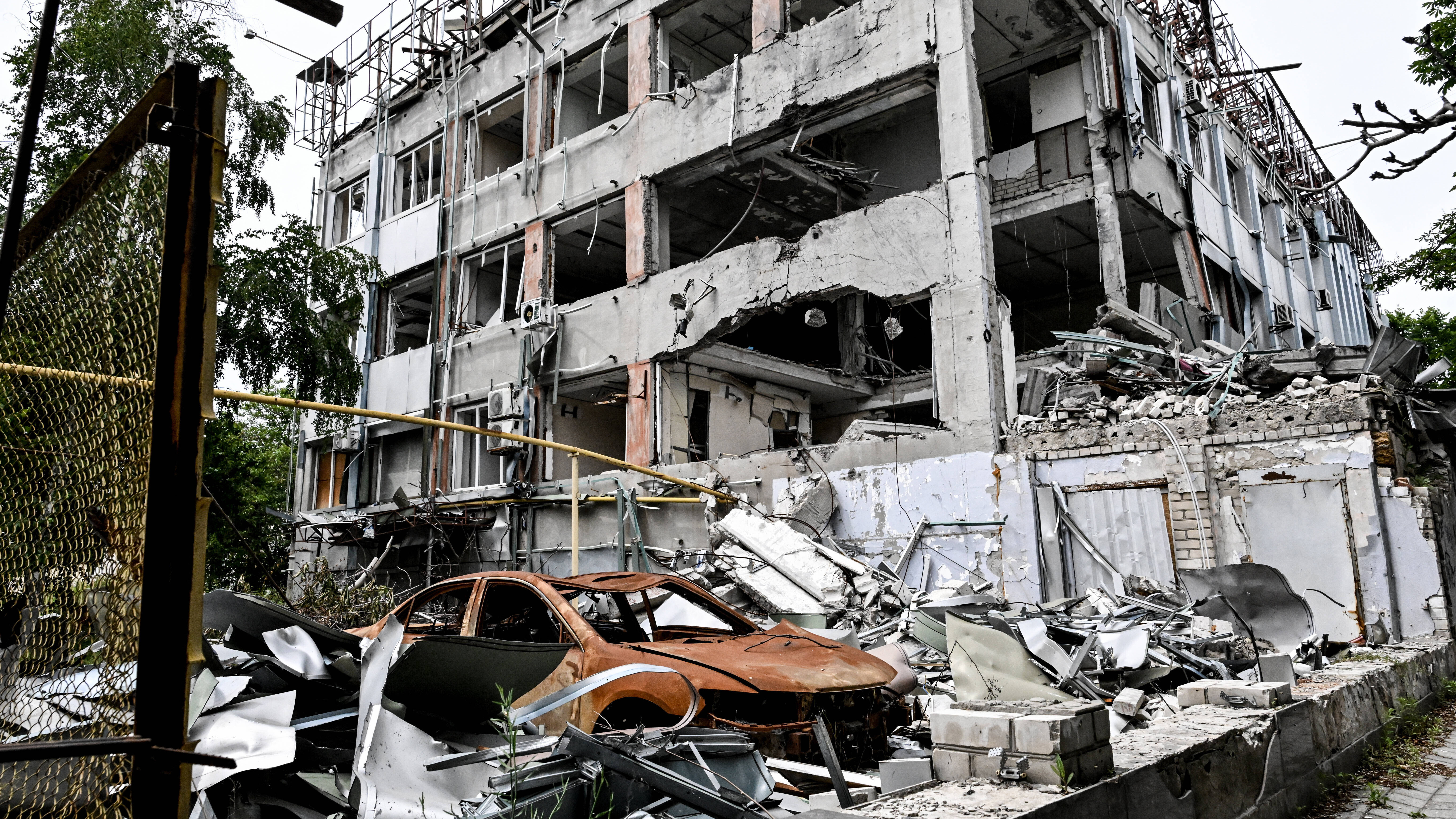 Durch russische Angriffe zerstörtes mehrstöckiges Wohnhaus und ausgebranntes rotes Autowrack (10.06.2026)