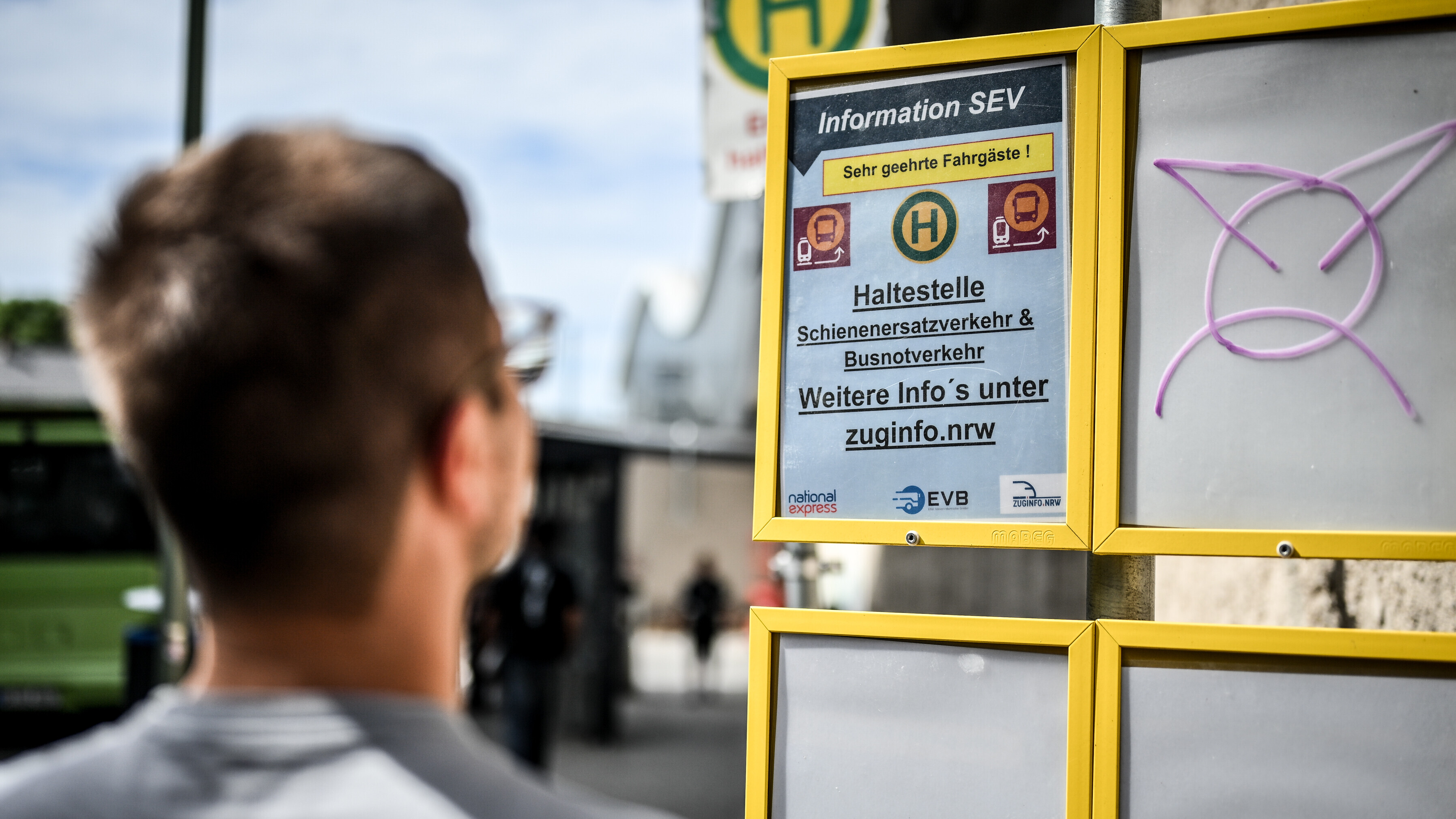 Ein Mann steht vor einem Schild, mit dem auf den Schienenersatzverkehr hingewiesen wird.