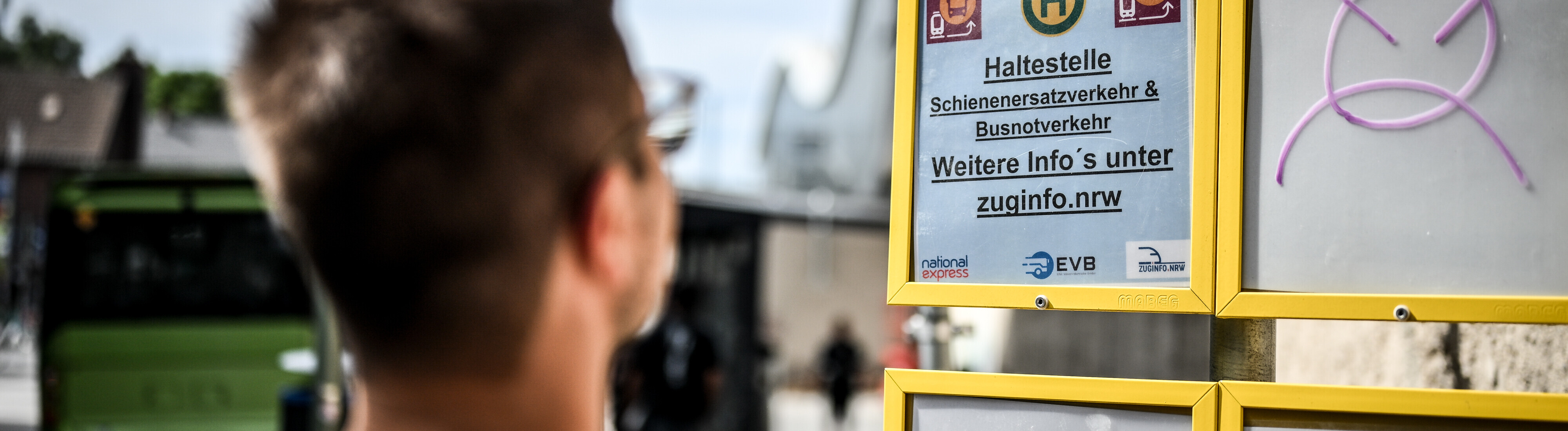 Ein Mann steht vor einem Schild, mit dem auf den Schienenersatzverkehr hingewiesen wird.