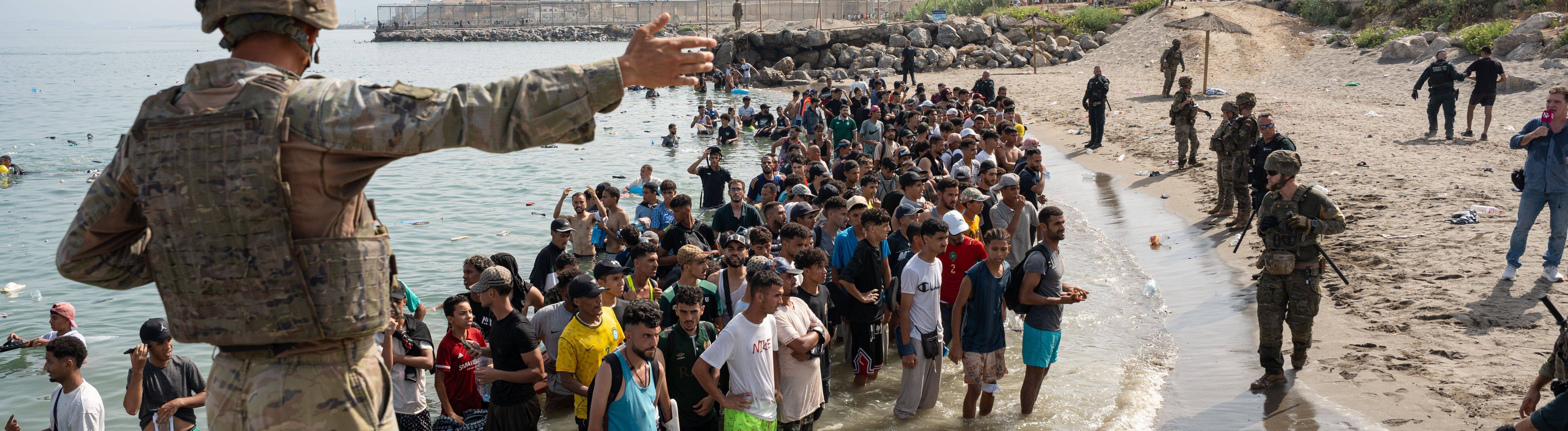 Geflüchtete stehen am Strand von Ceuta. Sie sind über das Meer von der marokkanischen Küste zu der spanischen Enklave geschwommen. Ein Soldat zeigt ihnen den Weg.