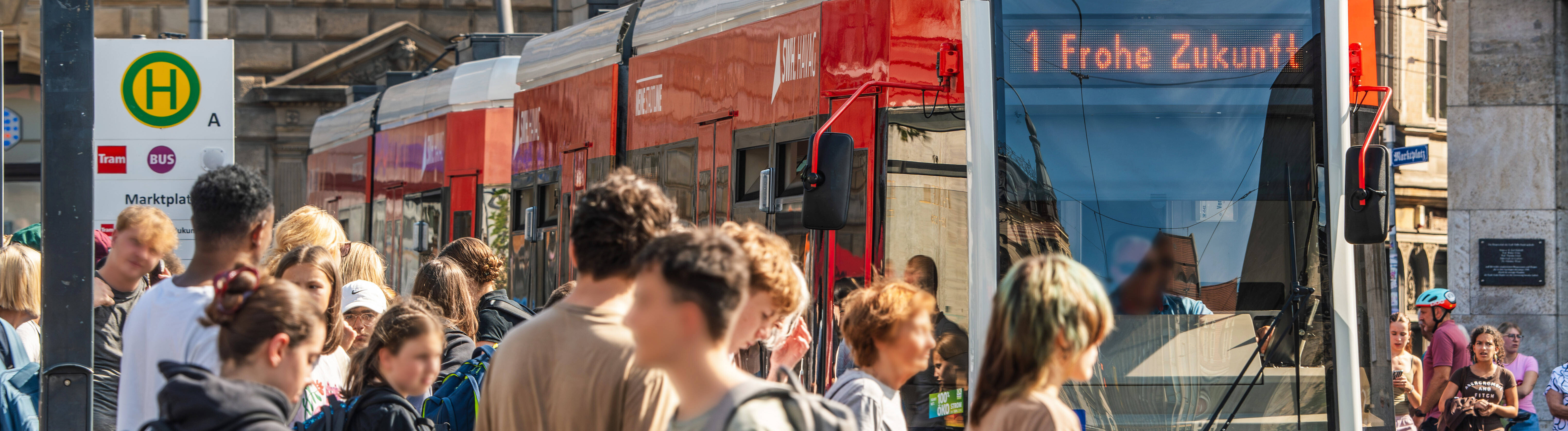 Menschen gehen an der Haltestelle Marktplatz vorbei, an der die Straßenbahn Linie 1 in Richtung Frohe Zukunft hält (Halle, 27.08.2026)