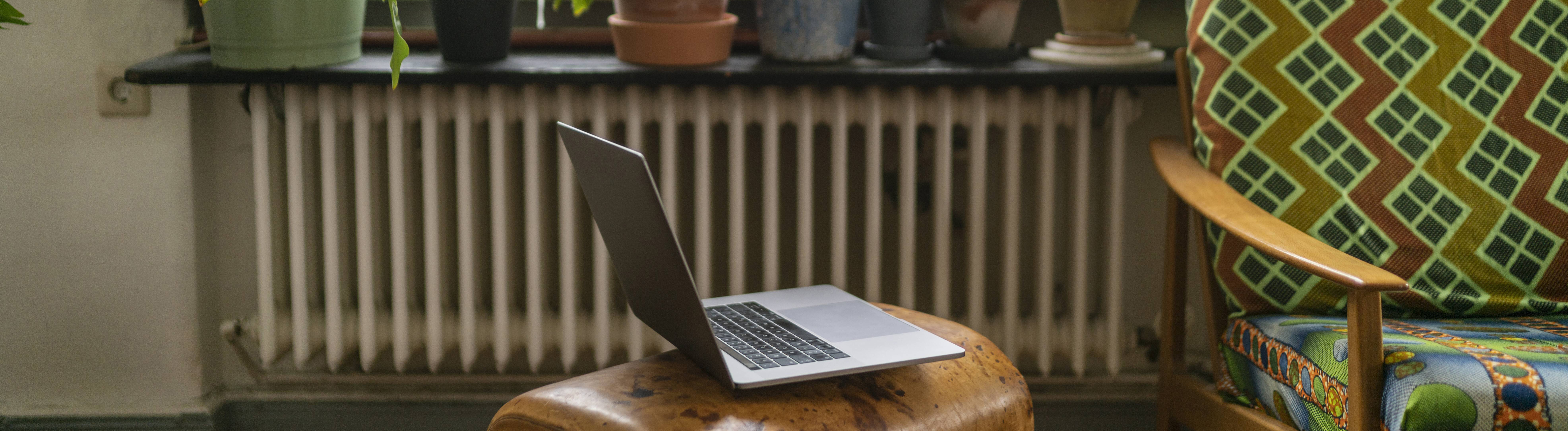 Ein Laptop neben einer Couch. Im Hintergrund Pflanzen auf der Fensterbank.