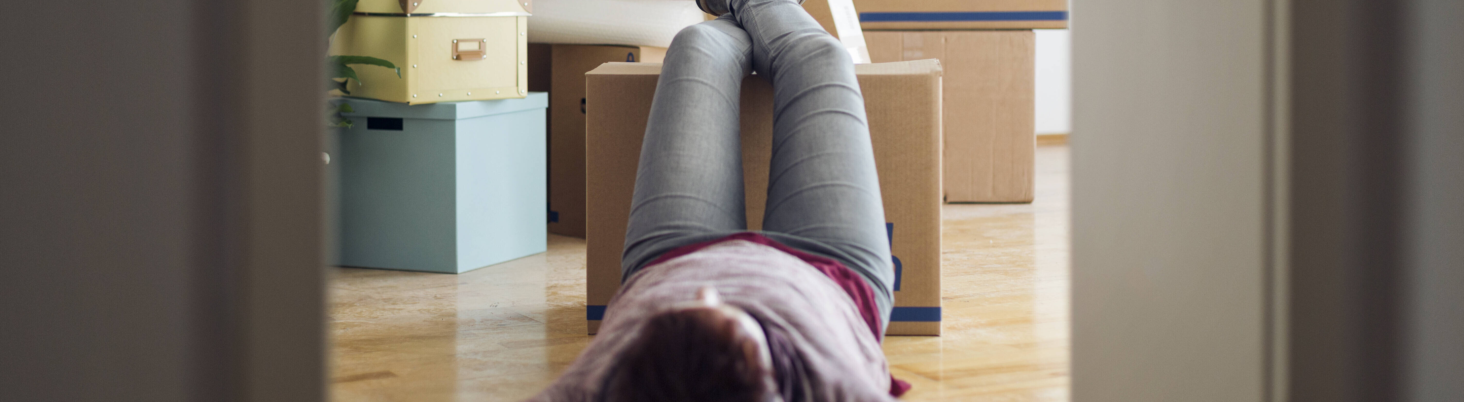 Eine Frau legt Pause bei ihrem Umzug ein. Sie liegt am Boden und hat die Beine auf einen Umzugskarton gelegt.