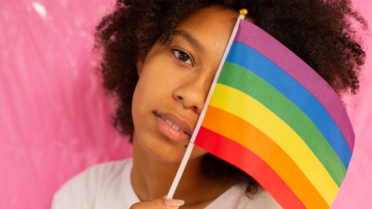 Eine Frau hält eine LGBTQI+ Flagge vor ihr Gesicht