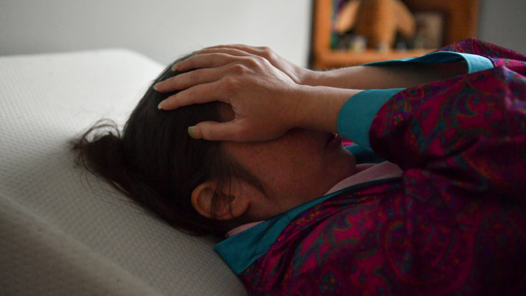 Eine Frau liegt auf einem Bett und schlägt die Hände vor ihr Gesicht