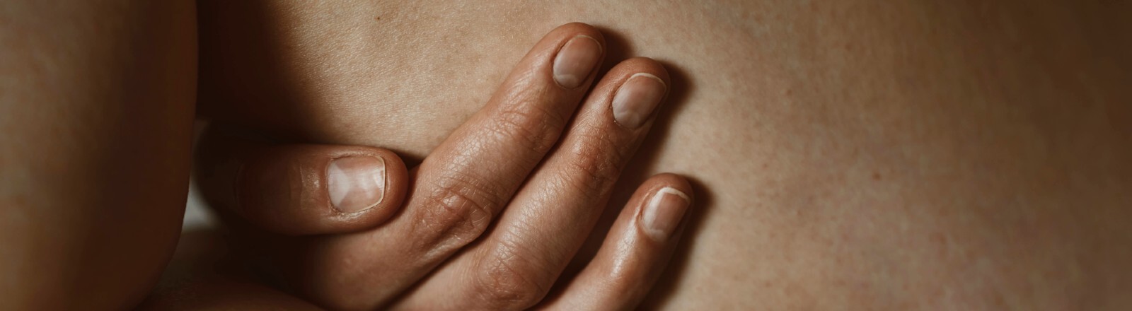 Eine Hand berührt einen nackten Oberschenkel. Das Bild zeigt eine Nahaufnahme.