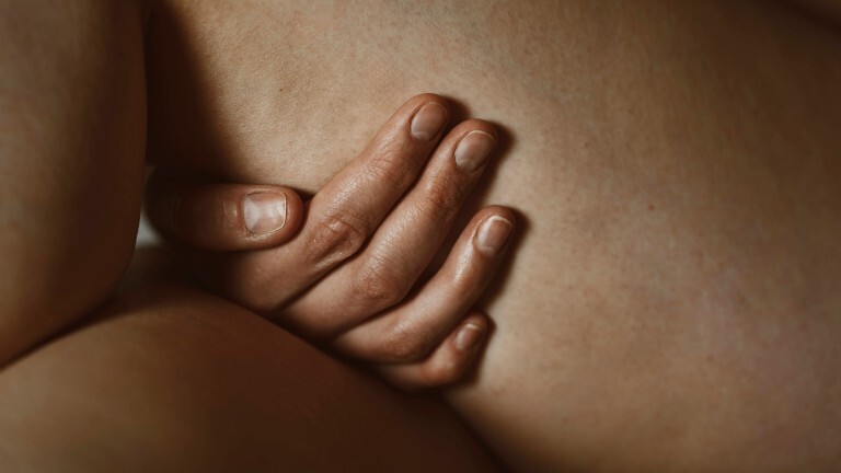 Eine Hand berührt einen nackten Oberschenkel. Das Bild zeigt eine Nahaufnahme.