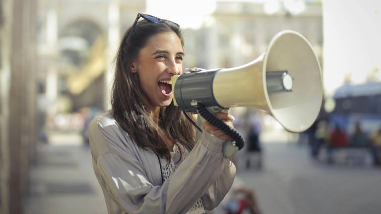 Frau spricht über ein Megaphone und lächelt dabei.