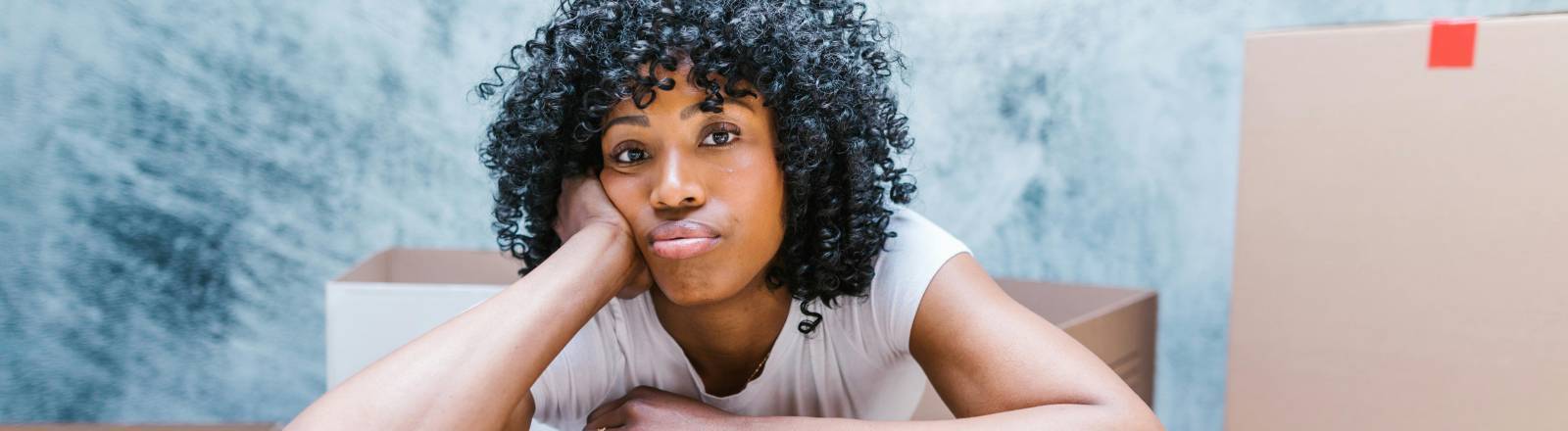 Frau stützt sich auf ihrem Ellenbogen auf einem Umzugskarton ab.