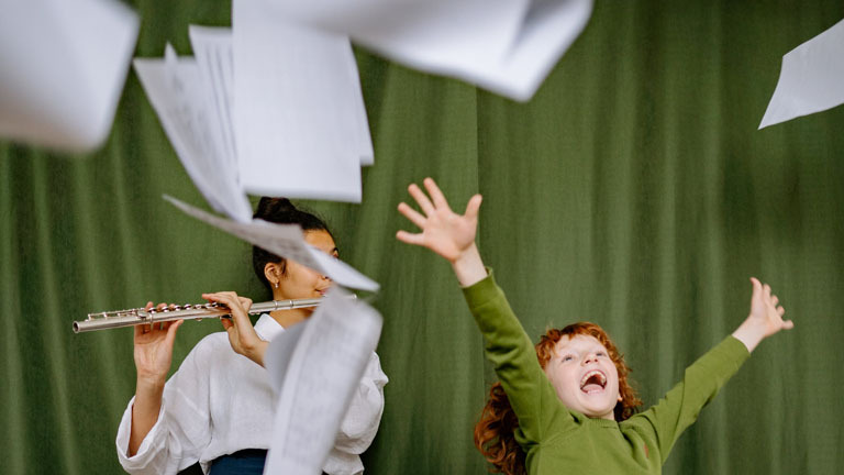 Frau spielt Klarinette, Junge wirft Notenblätter in die Luft