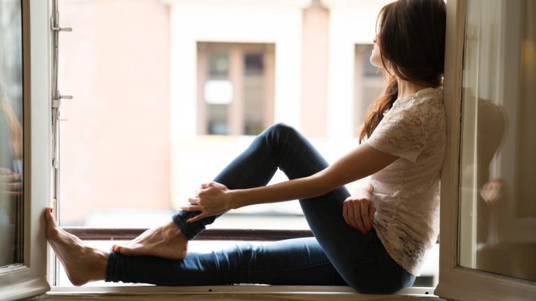 Frau sitzt auf Fensterbank und blickt aus dem offenen Fenster.