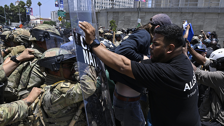 Foto eines Protestierenden in Los Angeles, der inmitten eines Handgemenges zwischen demonstrierenden und Sicherheitskräften im Rahmen der Proteste gegen die Abschiebepolitik Trumps das Schutzschild eines National-Guard-Soldaten wegschiebt