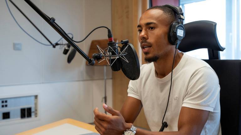 Der Fußballspieler Robin Afamefuna sitzt im Dlf Nova-Studio am Mikrofon und hat einen Kopfhörer auf.