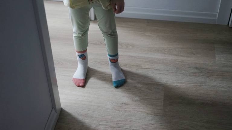 Ein kleines Mädchen, das verschiedene Socken trägt. steht an der Tür zwischen Flur und Schlafzimmer.