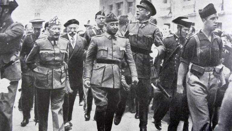 Schwarz-Weiß-Fotografie aus dem August 1936: General Francisco Franco schreitet in Burgos flankiert von den Generälen Emilio Mola, Miguel Cabanellas und José Cavalcanti durch eine Straße.