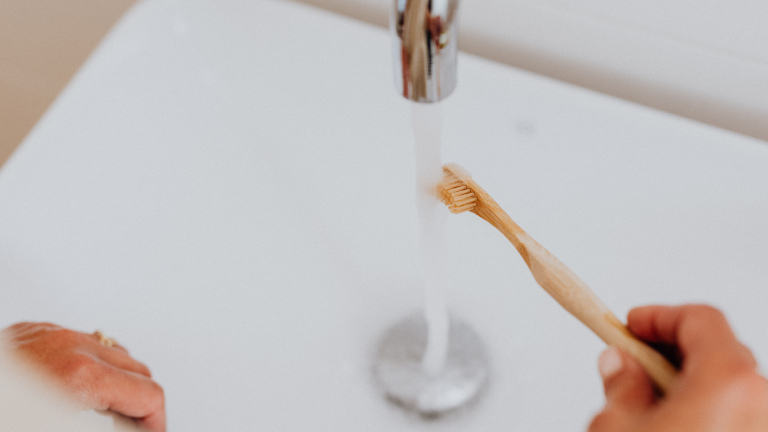 Ein Mensch hält die Zahnbürste unter Wasser