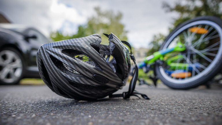 Symbolfoto zum Thema Fahrradunfall (gestellte Szene). Ein zerbrochener Fahrradhelm liegt neben einem Fahrrad auf einer Straße. Berlin, 21.08.2024.