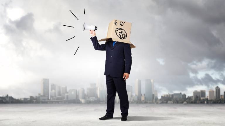 Ein Symbolbild eines verärgerten Geschäftsmanns. Er hält eine Flüstertüte in der Hand und trägt einen Karton auf dem Kopf.