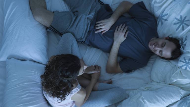 Ein Paar verbringt Zeit im Bett. Frau sitzt. Mann liegt und entspannt.