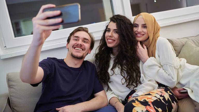 Drei Personen sitzen auf dem Sofa und machen ein Selfie. Die Frau (rechts im Bild) trägt ein Kopftuch als Zeichen ihrer Religiosität.
