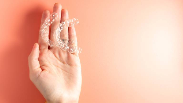 Zwei Ausrichtungshilfen/Zahnspangen gegen Zähneknirschen liegen auf der Hand einer Frau. Hintergrund der Hand ist orange.