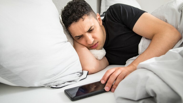 Ein Mann liegt im Bett und stellt seinen Smartphone-Wecker auf Snooze