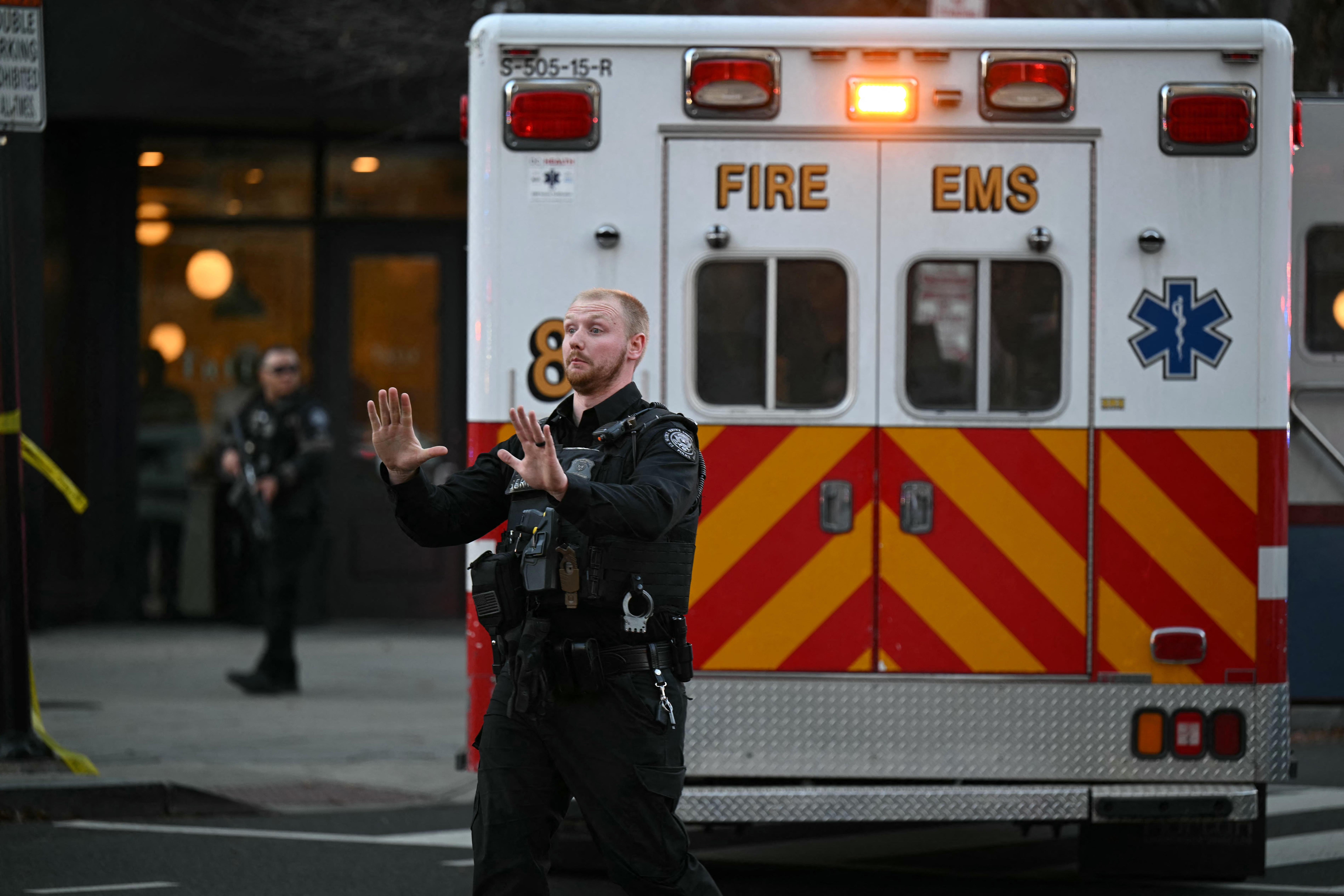 Ein amerikanischer Polizist steht vor einem Krankenwagen und gestikuliert. Die Türen des Fahrzeugs sind geschlossen. Nur seine Rückseite ist zu sehen.
