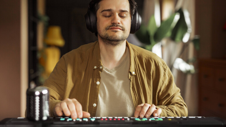Ein Mann sitzt an einem Keyboard und trägt dabei Kopfhörer. Sein Augen sind geschlossen.