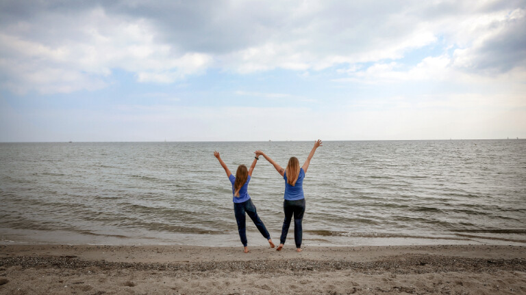 Zwei Frauen stehen am Strand, sie strecken die Arme in den Himmel