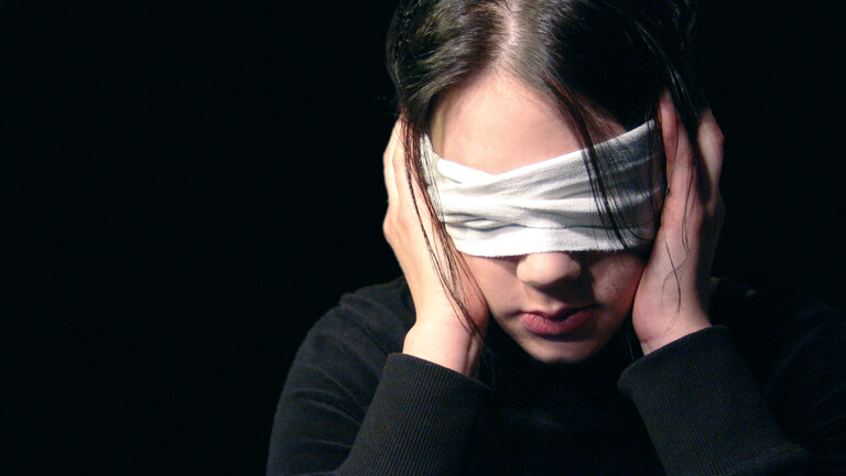 Eine Frau hält sich die Ohren zu und hat die Augen verbunden.