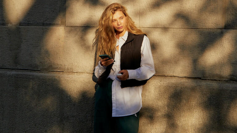 Eine Frau steht wartend am Straßenrand und schaut auf ihr Handy.