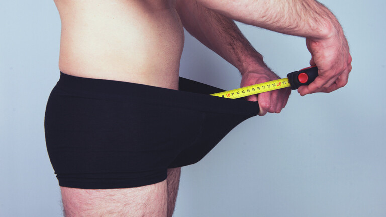 Mann hält Maßband in seine Unterhose