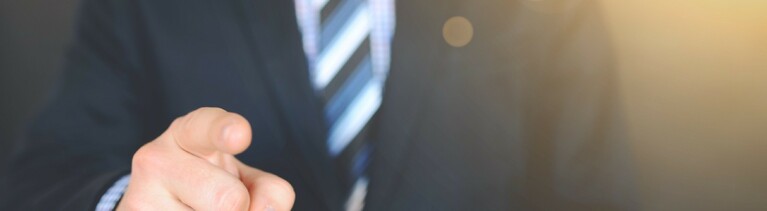 Ein Mann im Anzug zeigt mit dem Zeigefinger Richtung Kamera