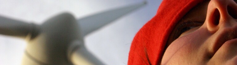 Eine Frau mit roter Mütze - im Hintergrund ein Windrad.