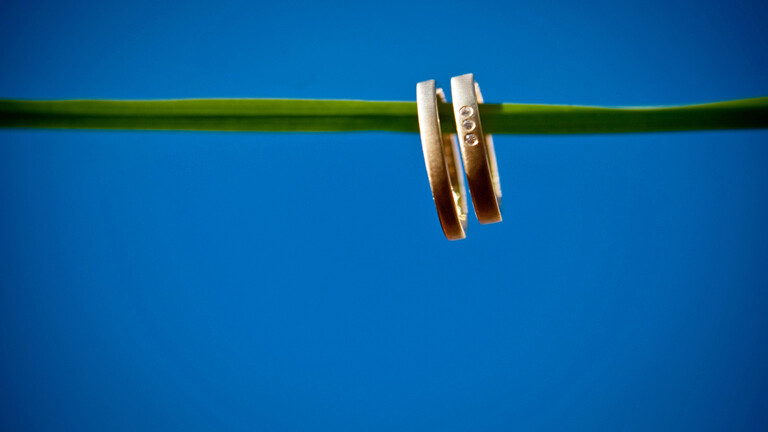 Zwei Eheringe sind auf einer grünen Schnur aufgereiht.