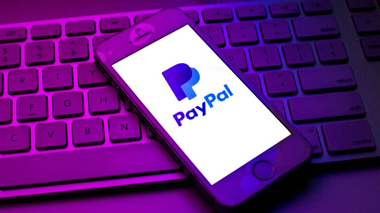 Ein Smartphone mit Paypal-Logo liegt auf einer Computertastatur.