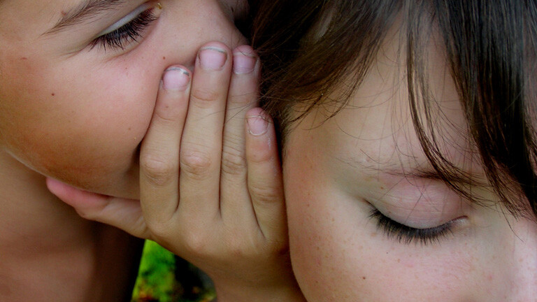 Ein Kind flüstert einem anderen etwas ins Ohr.