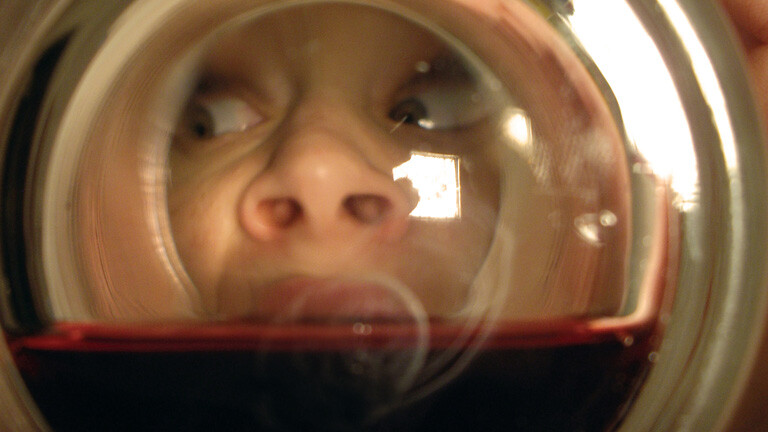 Frau schaut in Glas mit Rotwein, so dass man sie vom Glasboden sieht