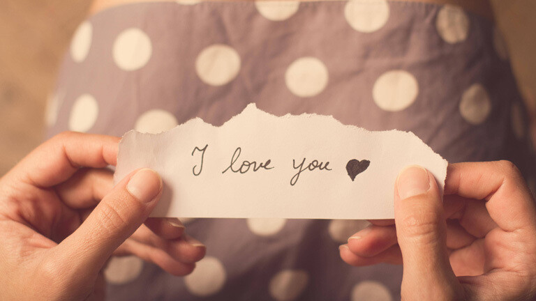 Frau hält Zettel mit den Worten "I love you" in der Hand