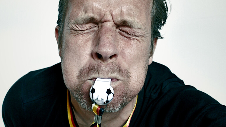 Schiedsrichter, der aus vollen Backen in die Trillerpfeife pustet